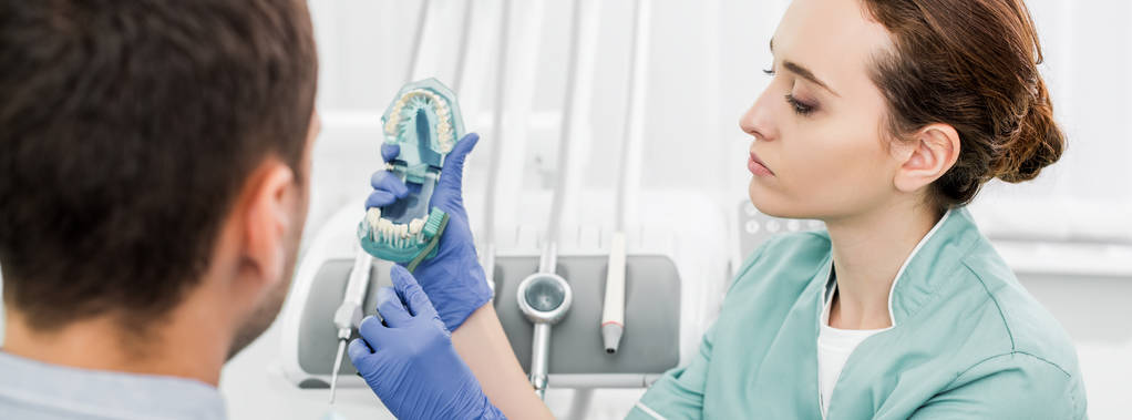 messa a fuoco selettiva del dentista femminile con modello di denti e spazzolino da denti vicino al paziente
 - Foto, immagini