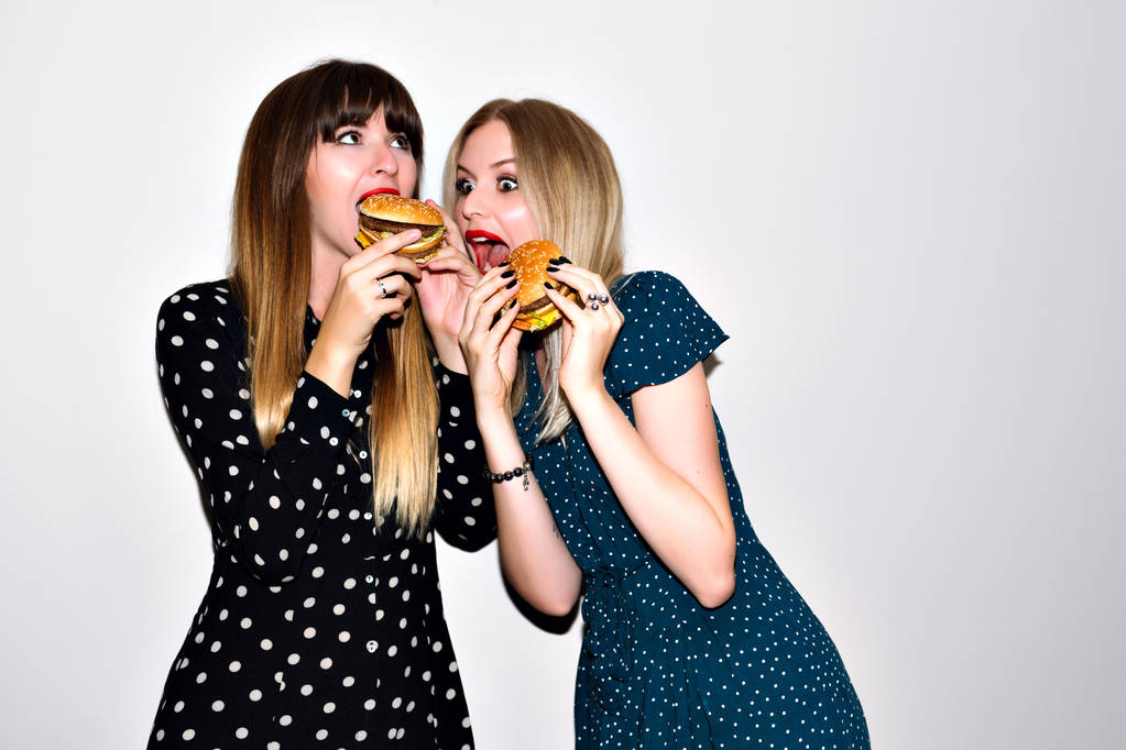 Lähikuva muoti elämäntapa muotokuva kaksi nuorta hipster tytöt syövät hampurilaisia
  - Valokuva, kuva