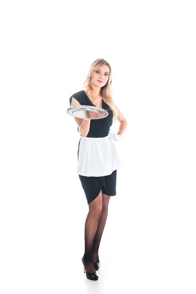 ελκυστική υπηρέτρια σε μαύρο ομοιόμορφη, ποδιά και κάλτσες στέκεται με θήκη σε λευκό φόντο - Φωτογραφία, εικόνα