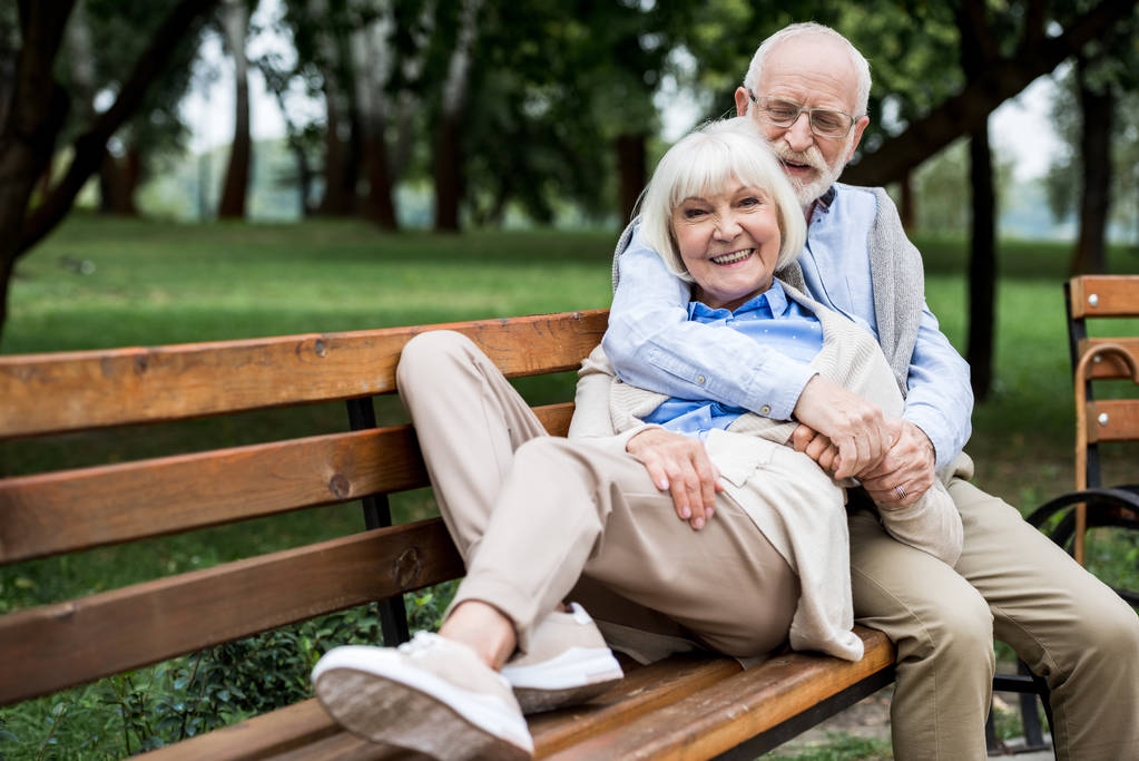 heureuse femme âgée posée sur le bouquet en bois près mari souriant dans le parc
  - Photo, image