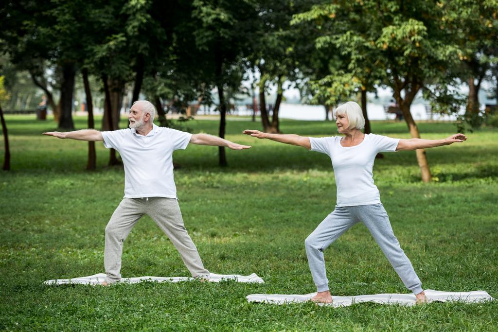 pareja mayor practicante guerrero II posa de pie sobre colchonetas de yoga
  - Foto, imagen