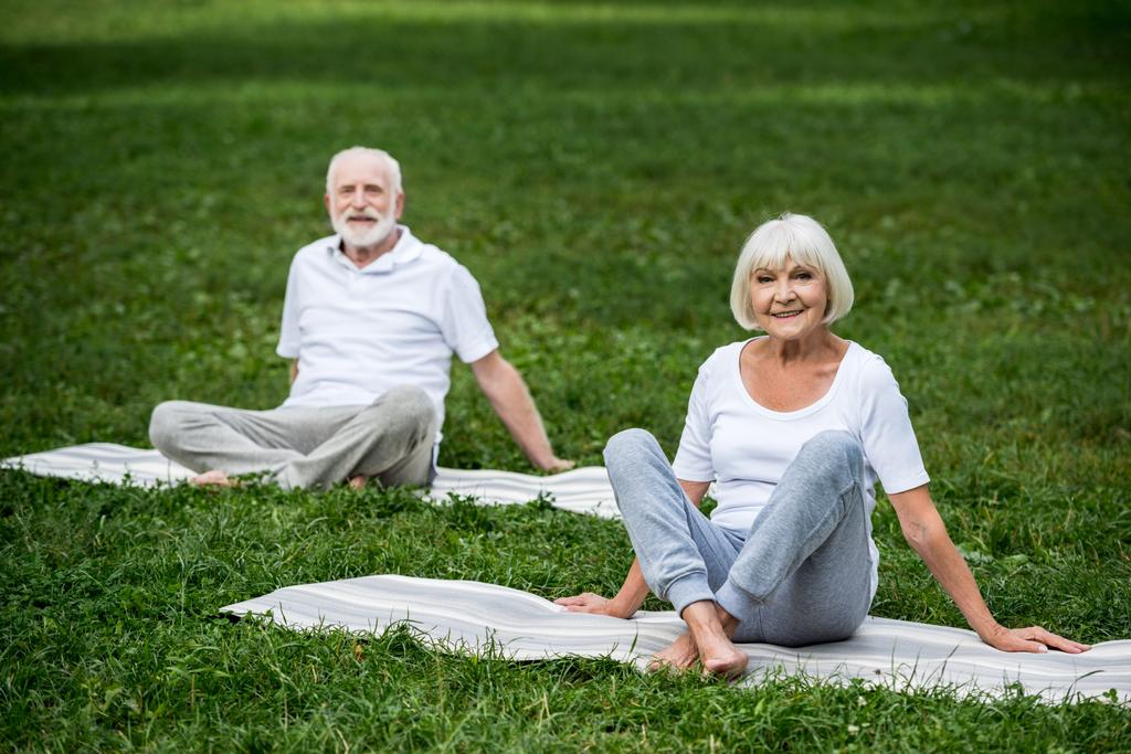 happy senior couple sitting in relaxation poses on yoga mats on green lawn  - Photo, Image