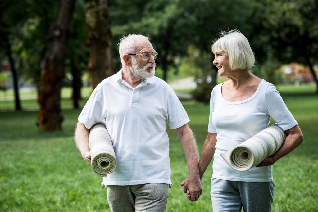 mutlu üst düzey çift ile parkta yürürken konuşmak fitness paspaslar - Fotoğraf, Görsel