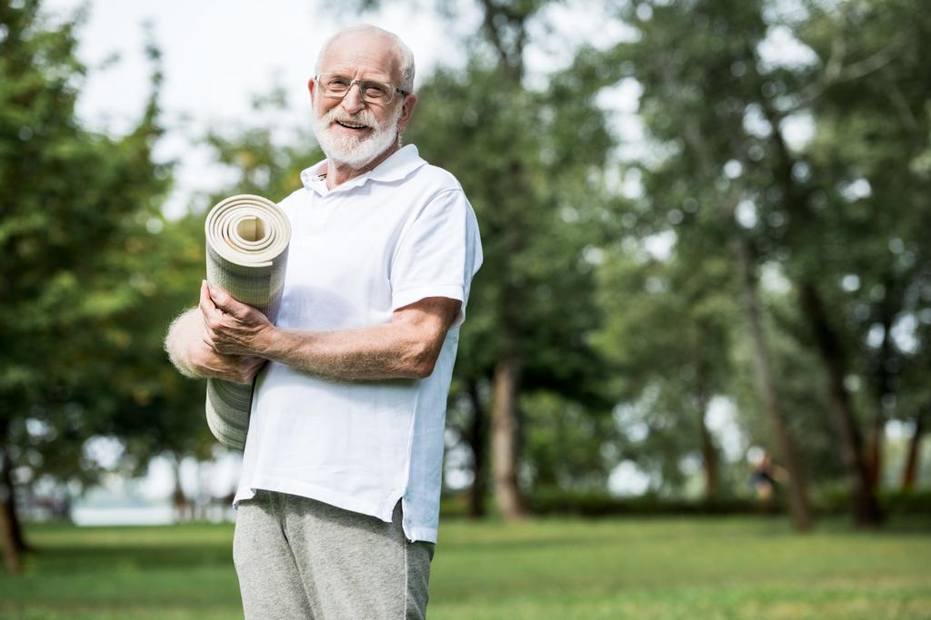 hombre mayor feliz con alfombra de fitness en el parque
 - Foto, imagen