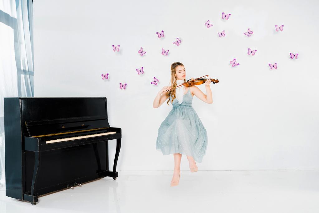 schwimmendes Mädchen in blauem Kleid spielt Geige auf weißem Hintergrund mit lila Schmetterlingen - Foto, Bild