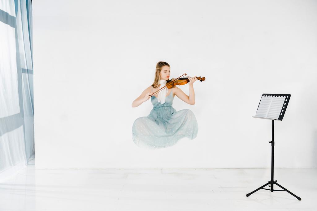 schwimmendes Mädchen in blauem Kleid spielt Geige mit Notenständer auf weißem Hintergrund  - Foto, Bild