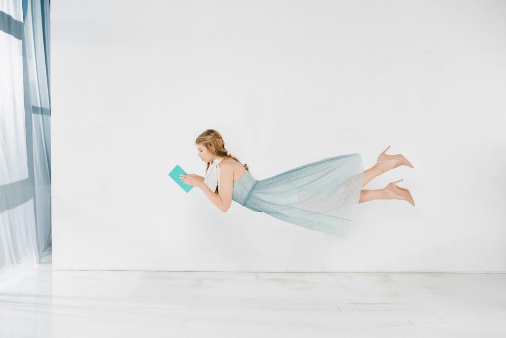 chica flotante en vestido azul libro de lectura en el aire con espacio de copia
 - Foto, imagen