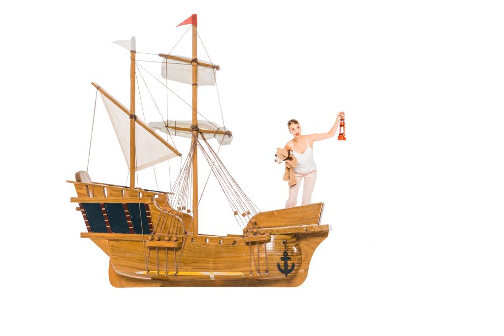 girl in pyjamas holding lantern, teddy bear and standing on floating ship model with copy space - Photo, Image