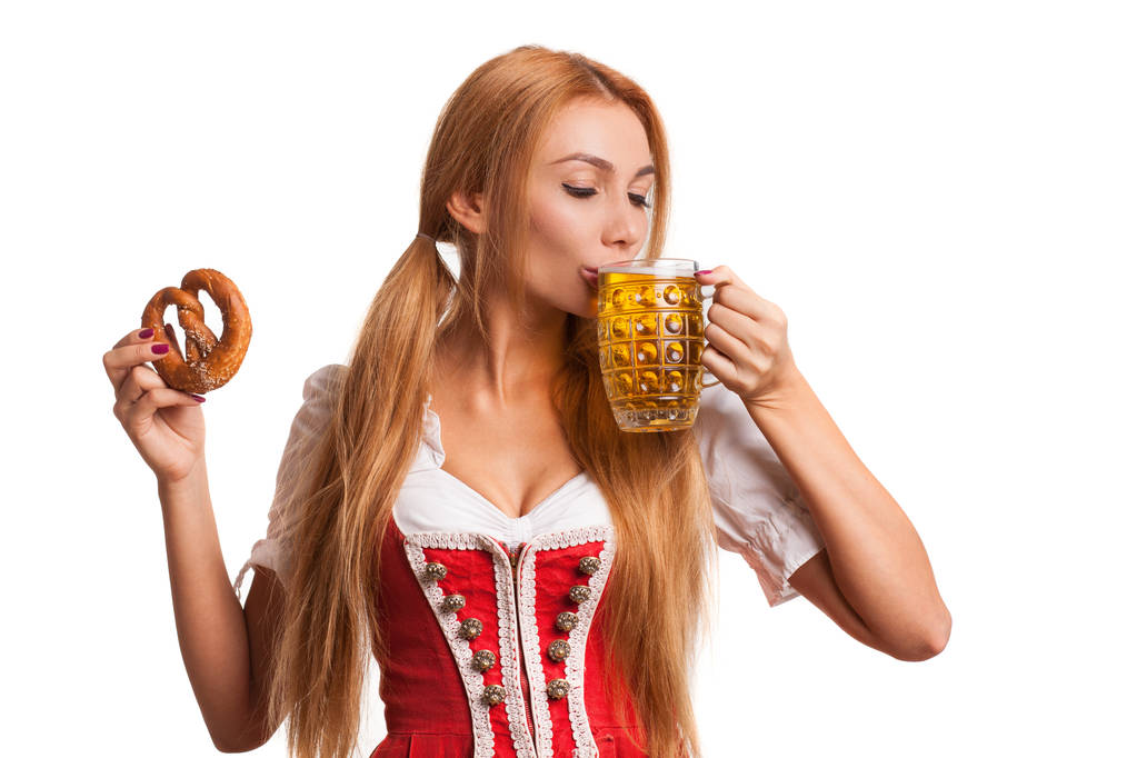 Portret van een prachtige sexy Beierse meisje heerlijk bier uit een mok, nippen krakeling, geïsoleerd op wit te houden. Vrolijke Okoberfest of St. Patriks serveerster drinken bier, kopie ruimte - Foto, afbeelding
