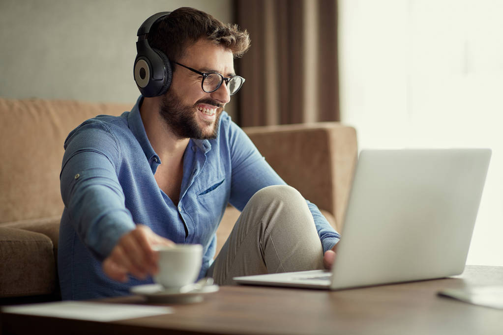 Homem sorridente usa um laptop para ouvir música e relaxar em casa
 - Foto, Imagem