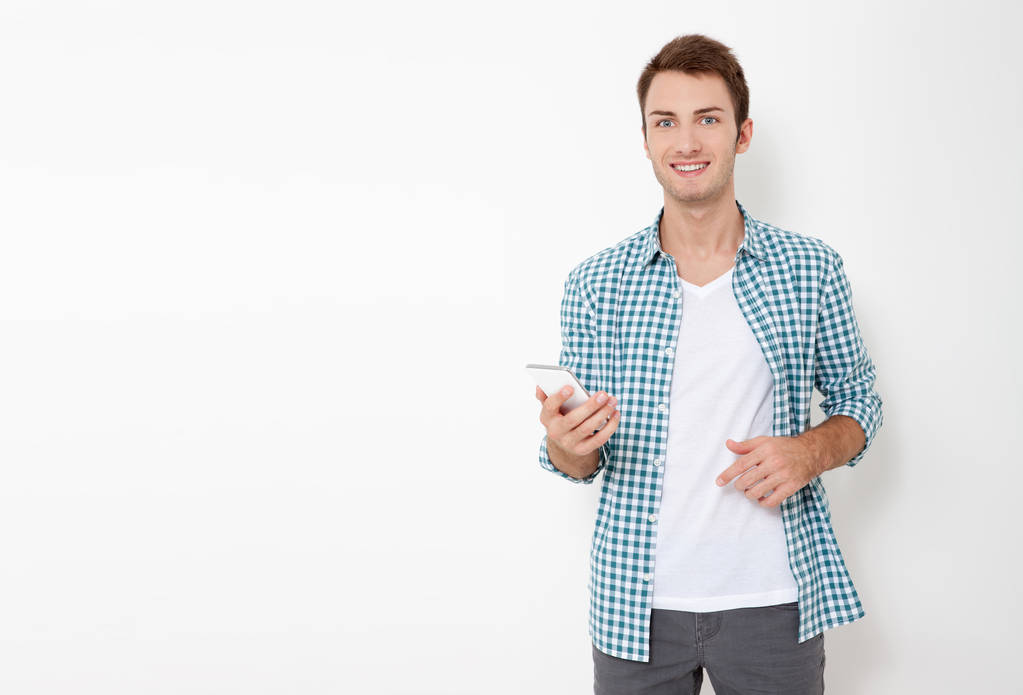 Hombre atractivo con pelo corto oscuro chateando o escribiendo mensaje de texto utilizando el teléfono celular aislado sobre fondo blanco - Foto, imagen