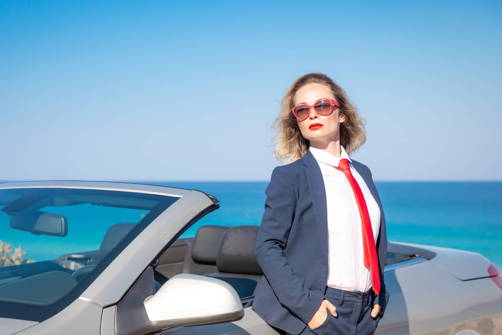 Úspěšná mladá podnikatelka na pláži. Žena stojící vedle klasické auto kabriolet. Letní prázdniny a svobodu cestování koncepce - Fotografie, Obrázek