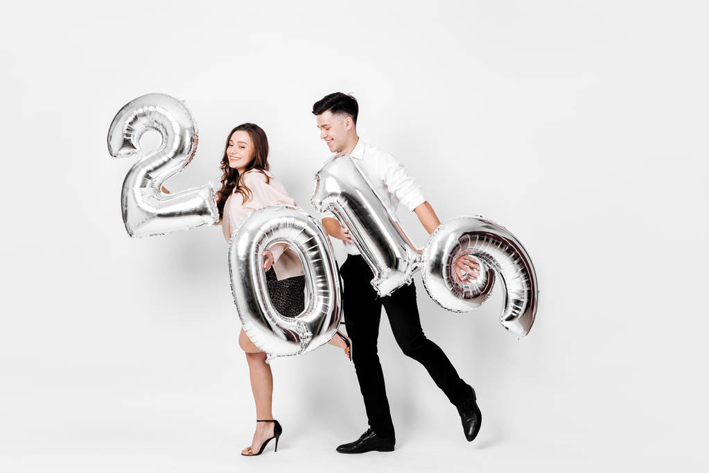 Ευτυχισμένος κορίτσι και άντρας ντυμένος με ένα κομψό έξυπνο ρούχα κρατούν μπαλόνια με τη μορφή των αριθμών 2019 σε λευκό φόντο στο στούντιο - Φωτογραφία, εικόνα