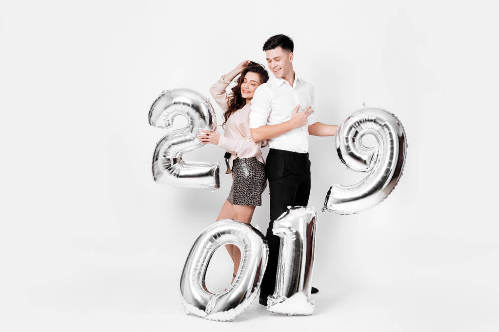 Κοπέλα και άντρας ντυμένος με ένα κομψό έξυπνο ρούχα κρατούν μπαλόνια με τη μορφή των αριθμών 2019 σε λευκό φόντο στο στούντιο - Φωτογραφία, εικόνα