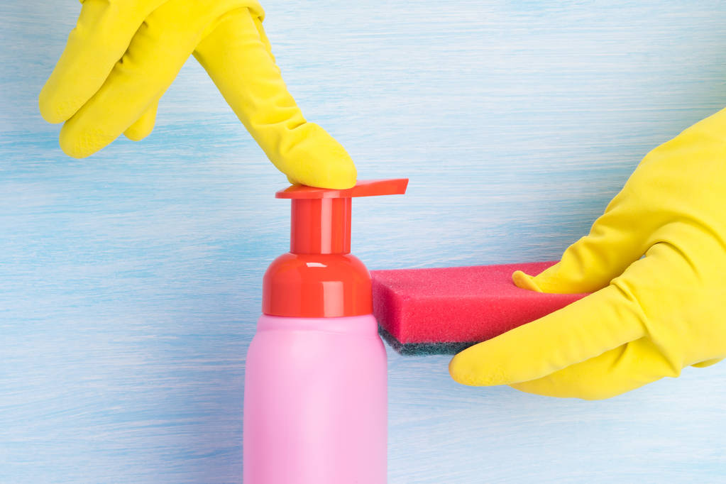 manos en guantes de goma de color amarillo verter líquido lavavajillas sobre una esponja sobre un fondo claro
 - Foto, imagen