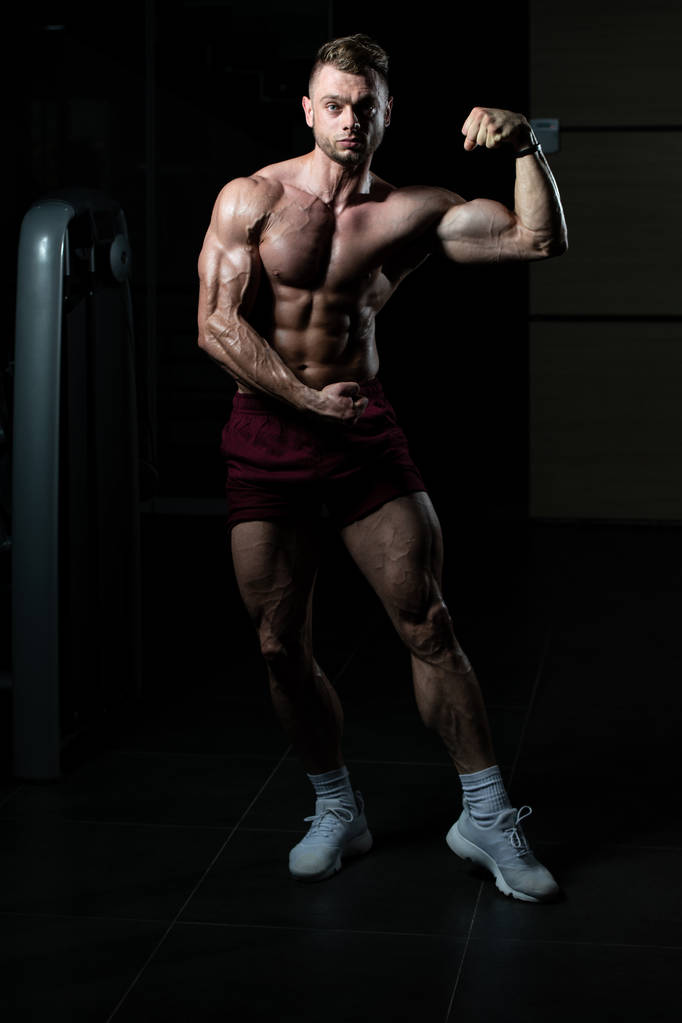 Красивий молодий чоловік стоїть сильним в тренажерному залі і гнучкі м'язи м'язи - м'язовий спортивний культурист фітнес-модель позування після вправ
 - Фото, зображення