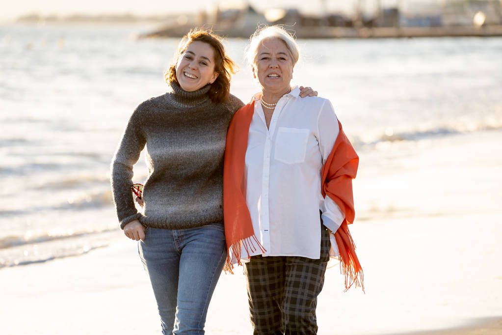 Retrato de madre mayor feliz e hija adulta pasando tiempo juntos tomados de la mano riendo y caminando en la playa a la luz del atardecer en momentos familiares felices Generaciones Retiro y concepto de personas
. - Foto, imagen