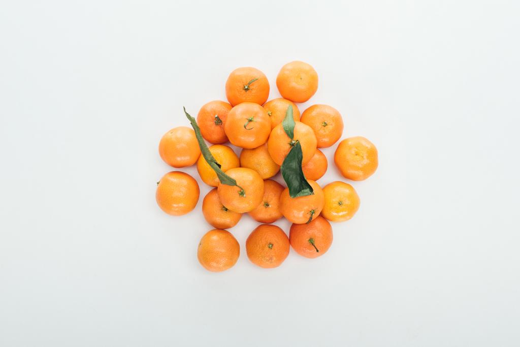 верхний вид ярких спелых оранжевых мандаринов с зелеными листьями, сложенными в кучу на белом фоне
 - Фото, изображение