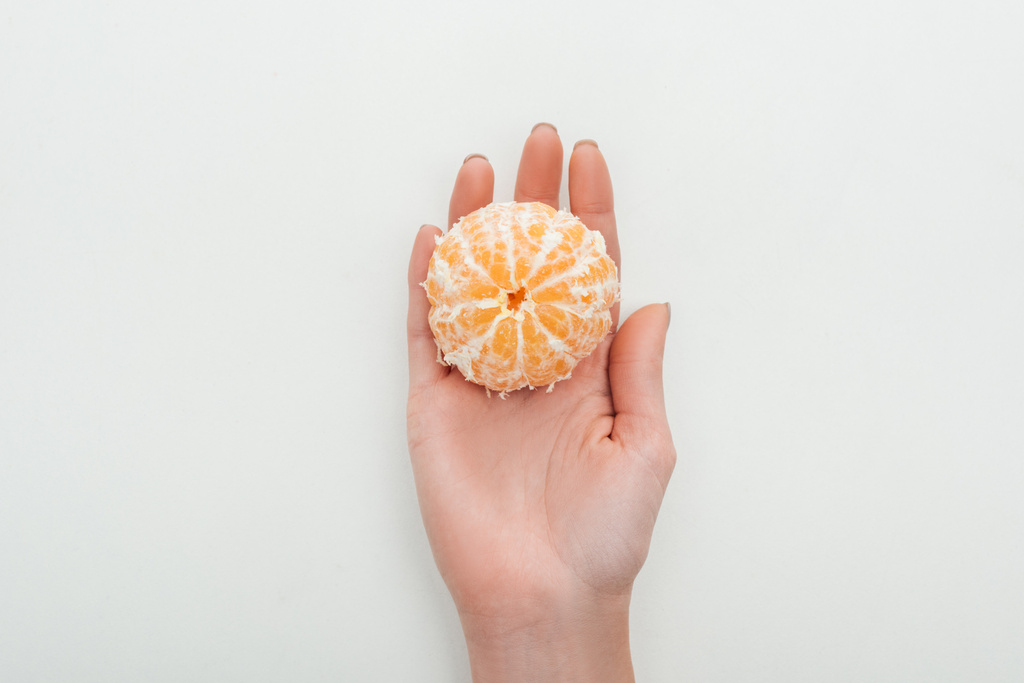 vue partielle de la femme tenant la mandarine entière pelée dans la paume sur fond blanc
 - Photo, image