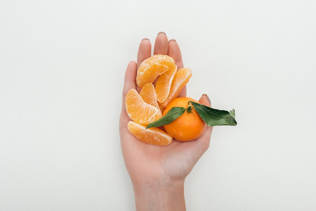bijgesneden beeld van vrouw met gepelde tangerine segmenten en hele tangerine op witte achtergrond - Foto, afbeelding