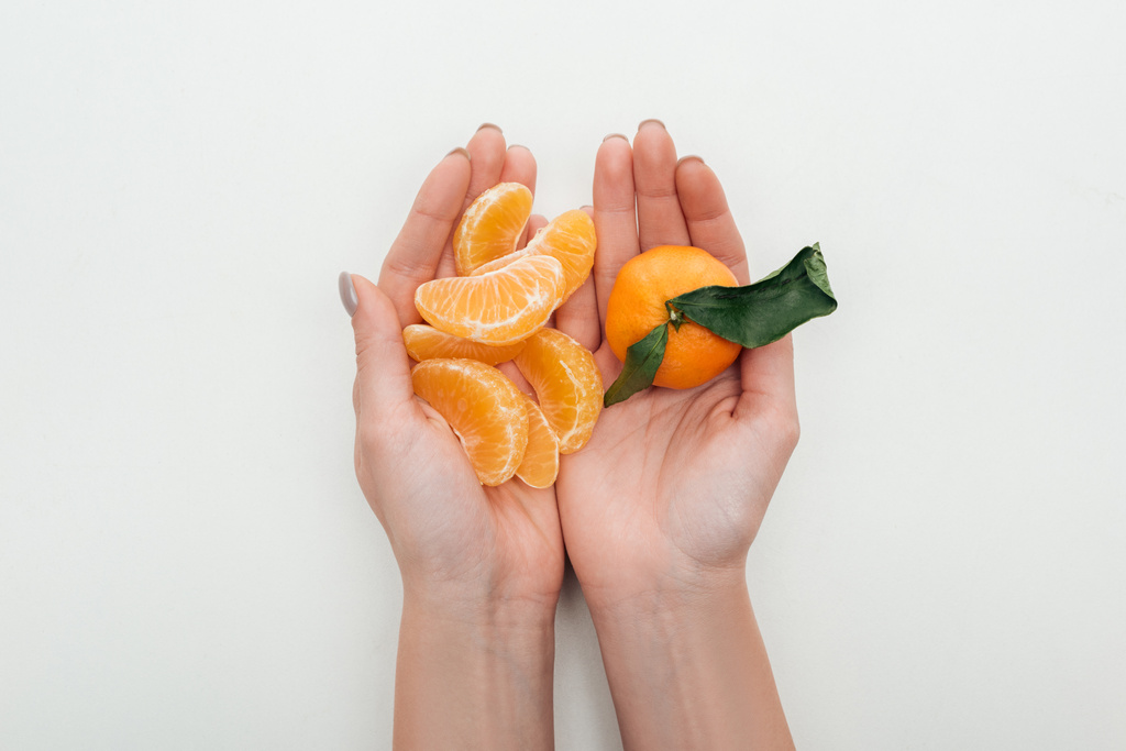 oříznutý pohled ženy držící oloupané mandarinky řezy a celé mandarinka na bílém pozadí - Fotografie, Obrázek