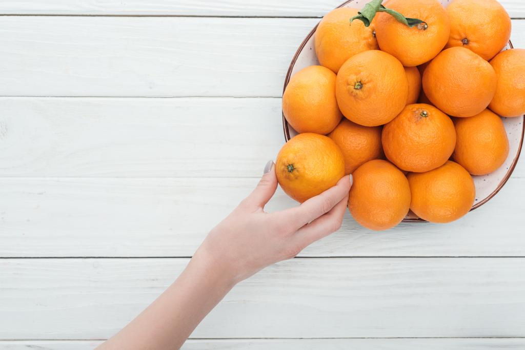 vista parziale della mano femminile vicino piatto con mandarini su sfondo bianco in legno con spazio copia
 - Foto, immagini