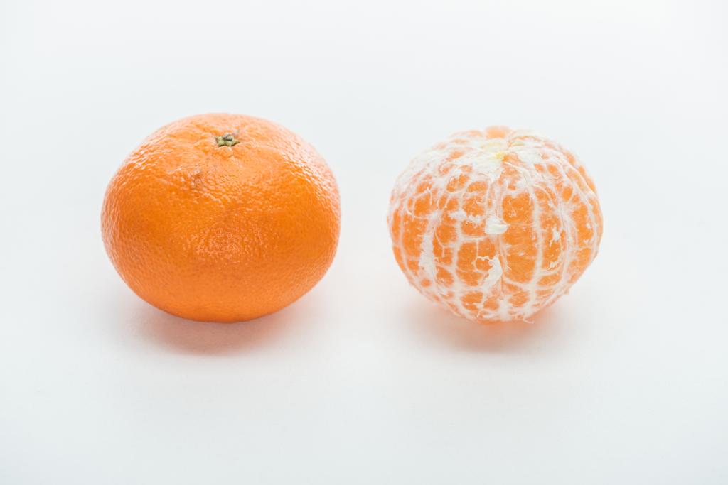 熟したオレンジ色全体が皮をむき、皮が付いたままのみかんにホワイト バック グラウンド - 写真・画像