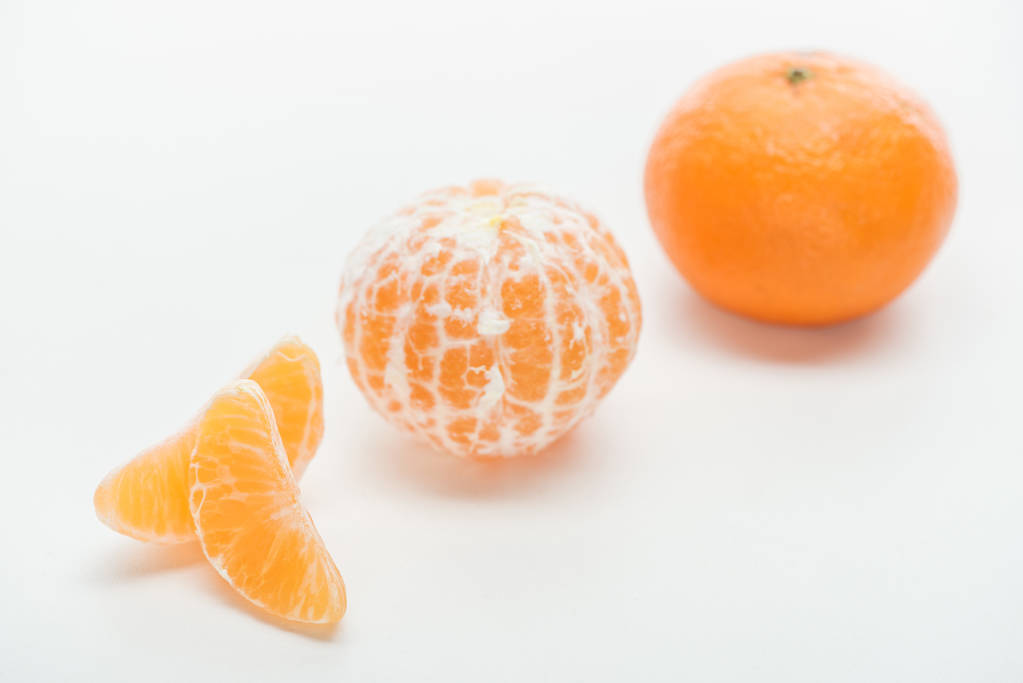 селективный фокус спелых апельсиновых целых очищенных и неочищенных мандаринов с ломтиками на белом фоне
 - Фото, изображение