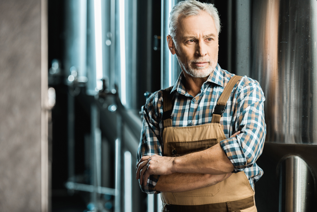 старший пивовар позирует со скрещенными руками в рабочем комбинезоне на пивоваренном заводе
 - Фото, изображение
