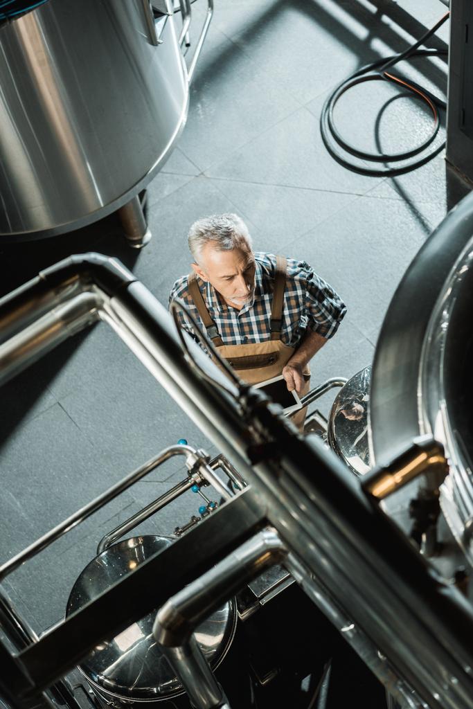 bovenaanzicht van mannelijke senior brouwer met behulp van digitale apparaat in brouwerij - Foto, afbeelding