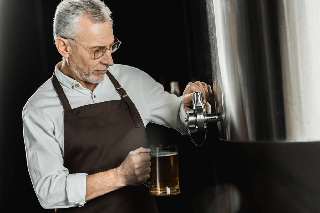 senior male brewer pouring beer into glass in brewery - Photo, Image