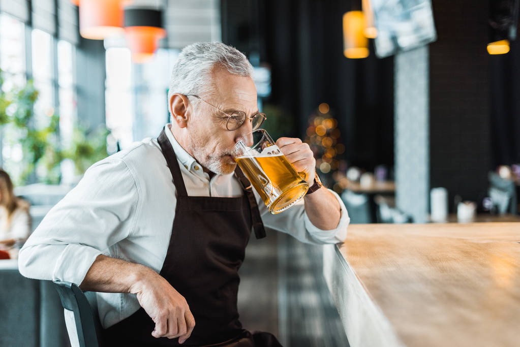 male worker in apron holding drinking beer in pub - Photo, Image
