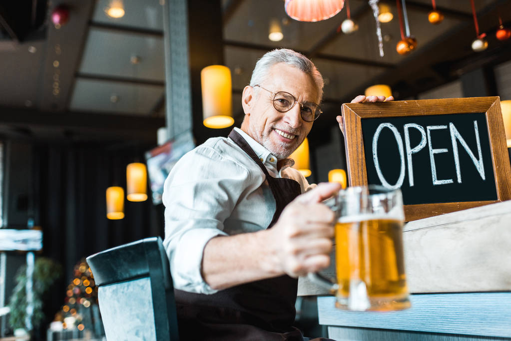 sonriente propietario senior de pub sosteniendo signo abierto y vaso de cerveza
 - Foto, imagen