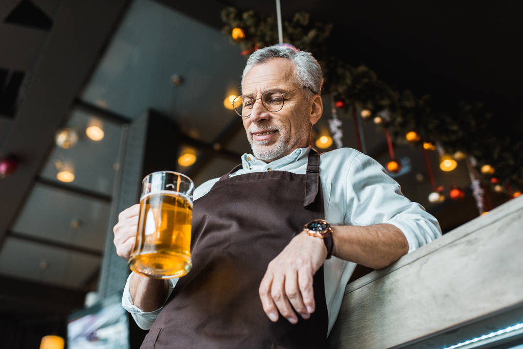 Arbeiter in Schürze hält Glas Bier in Kneipe - Foto, Bild