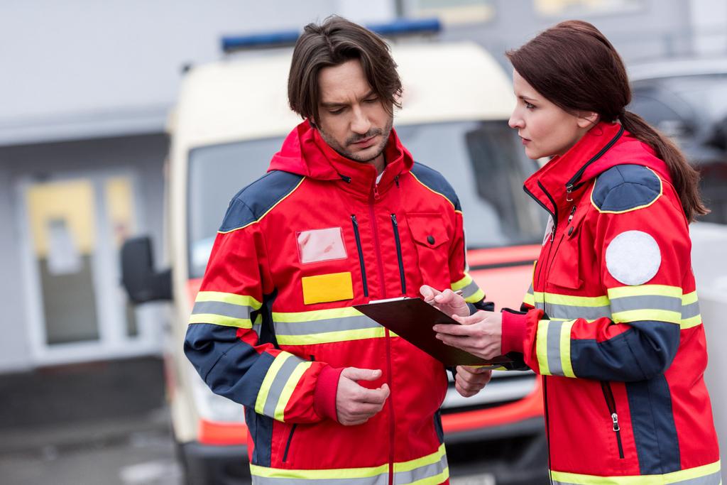 Ernstige paramedici in rode uniform lezen van notities in Klembord - Foto, afbeelding