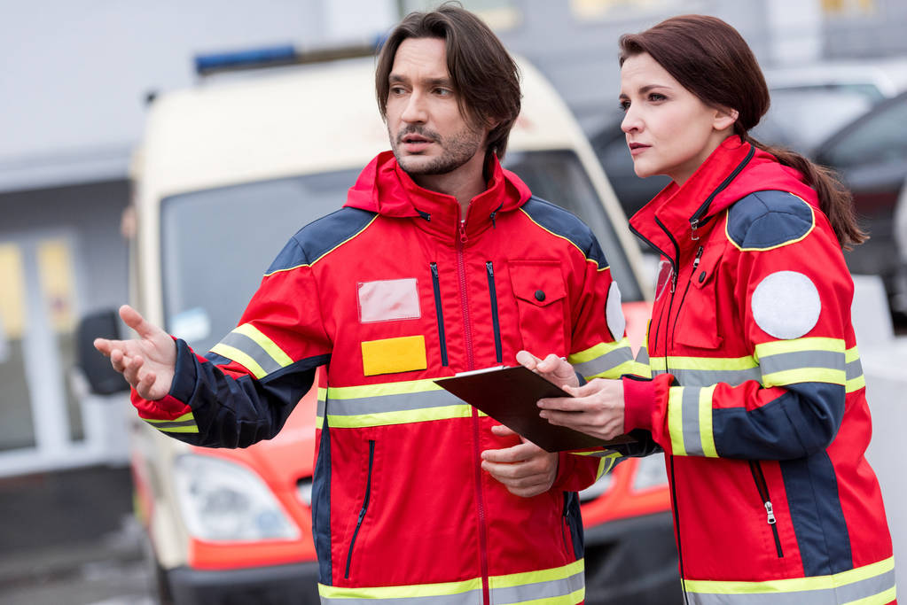 Sanitäter in roter Uniform reden und schauen auf der Straße weg - Foto, Bild