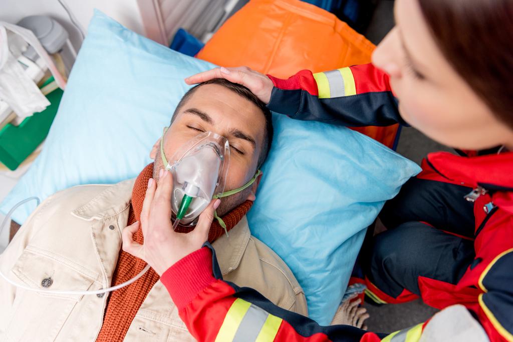 Ausgeschnittene Ansicht eines Sanitäters mit Sauerstoffmaske auf bewusstlosem Patienten - Foto, Bild