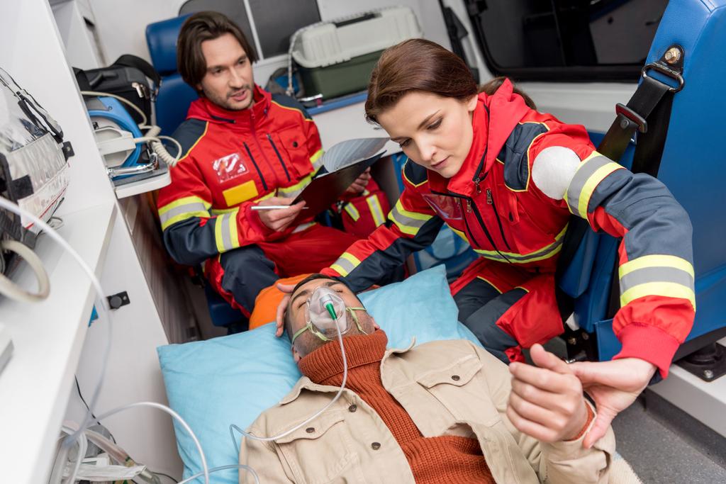 Oksijen maskesi hasta üzerinde tutarak ve nabız kontrol sağlık görevlisi - Fotoğraf, Görsel