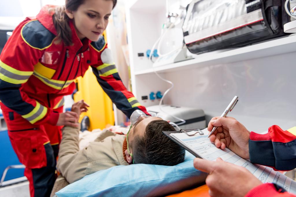 Weergave van paramedicus schrijven diagnose terwijl collega controleren pulse bijgesneden - Foto, afbeelding