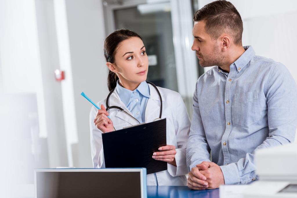 Μελαχρινή γιατρός με πρόχειρο μιλώντας στον ασθενή στο ιατρείο - Φωτογραφία, εικόνα
