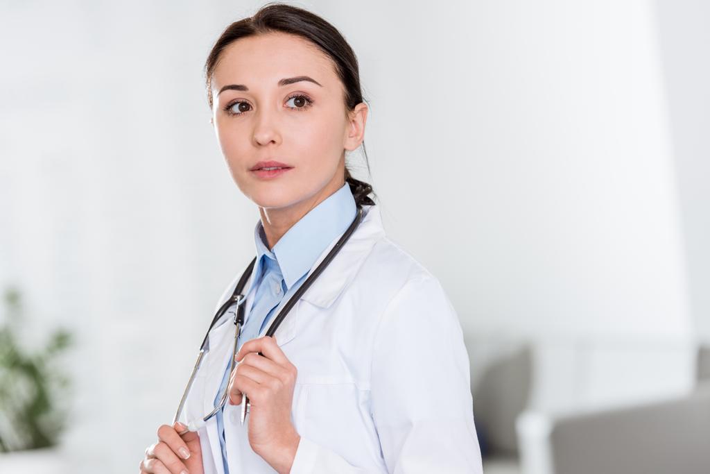 Médico femenino pensativo en bata blanca con estetoscopio mirando hacia otro lado
 - Foto, imagen
