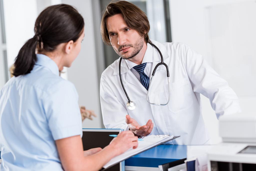 Vakava lääkäri stetoskoopilla puhuu sairaanhoitajan kanssa klinikalla
 - Valokuva, kuva