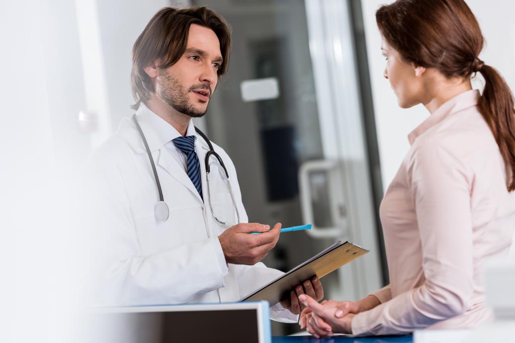 Doctor with clipboard talking to patient in clinic - Photo, Image