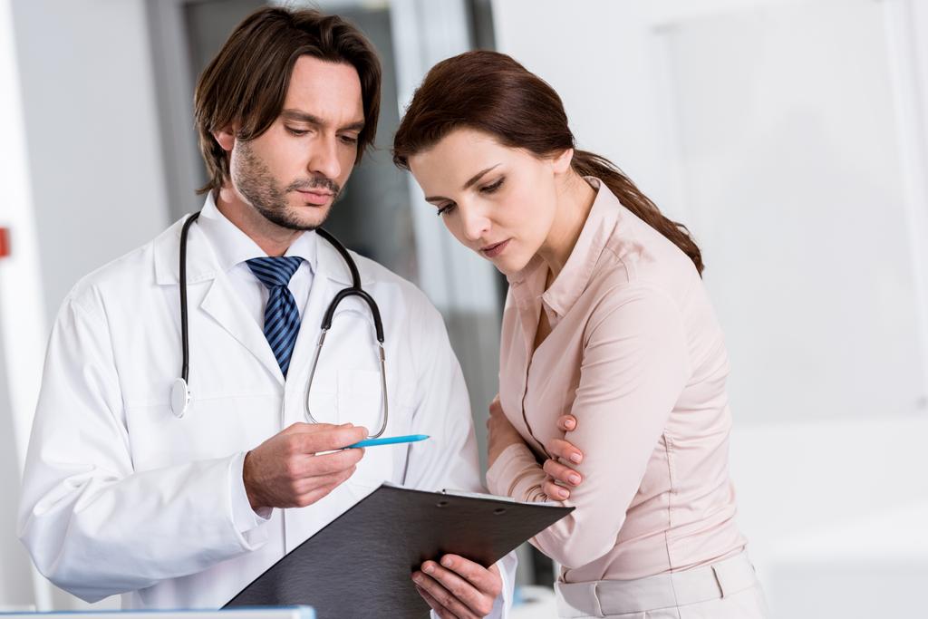Lekarz z stetoskop i pacjenta, ogląda schowka - Zdjęcie, obraz