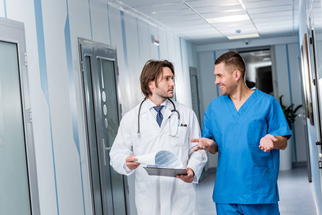 Doctor con portapapeles hablando con enfermera en uniforme azul
 - Foto, Imagen