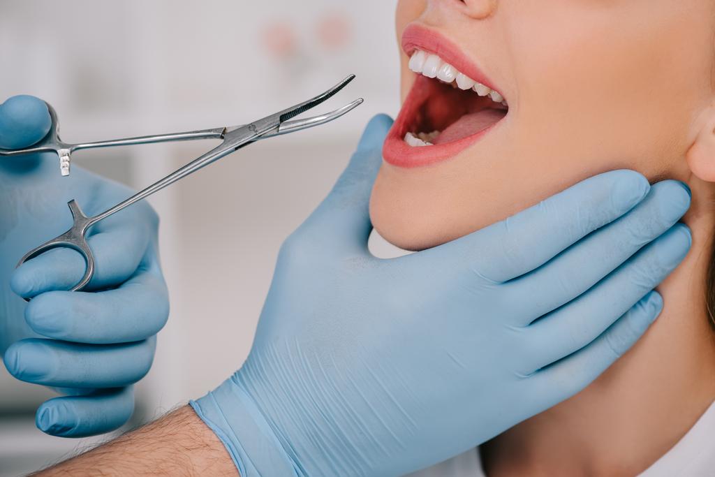 vista recortada del dentista en guantes de látex con instrumento dental examinando los dientes de la mujer en la clínica
 - Foto, imagen