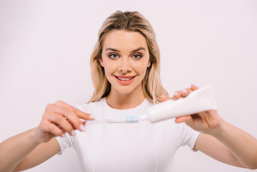 bella donna sorridente mettendo dentifricio sullo spazzolino isolato su bianco
 - Foto, immagini