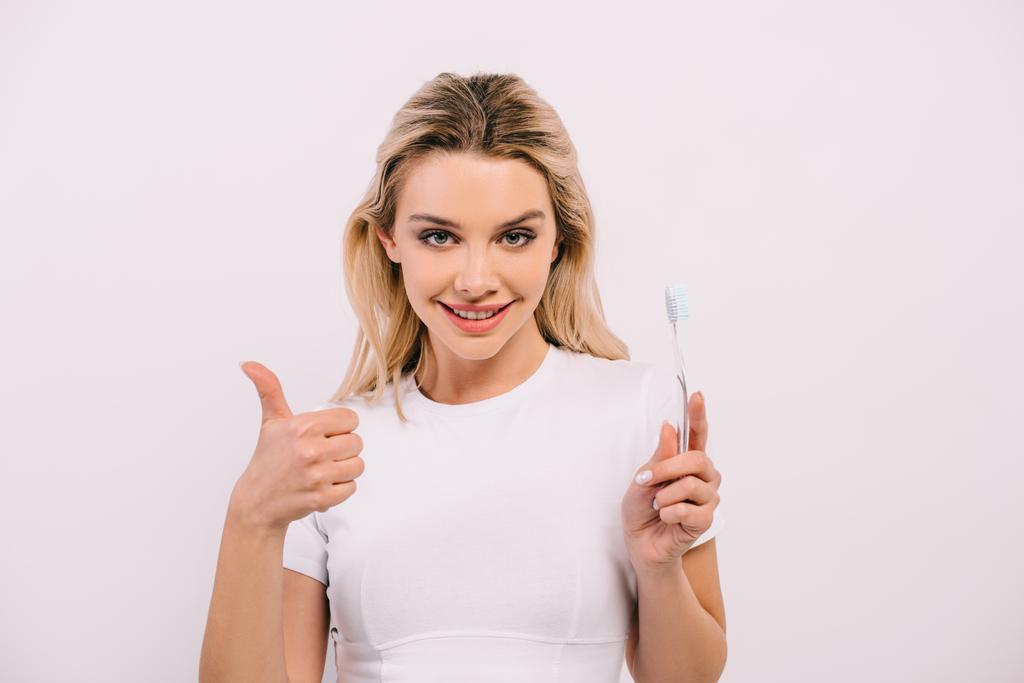 kaunis nainen valkoisessa paidassa tilalla hammasharja, katsot kameraa ja näytetään peukalo ylös merkki eristetty valkoinen
 - Valokuva, kuva
