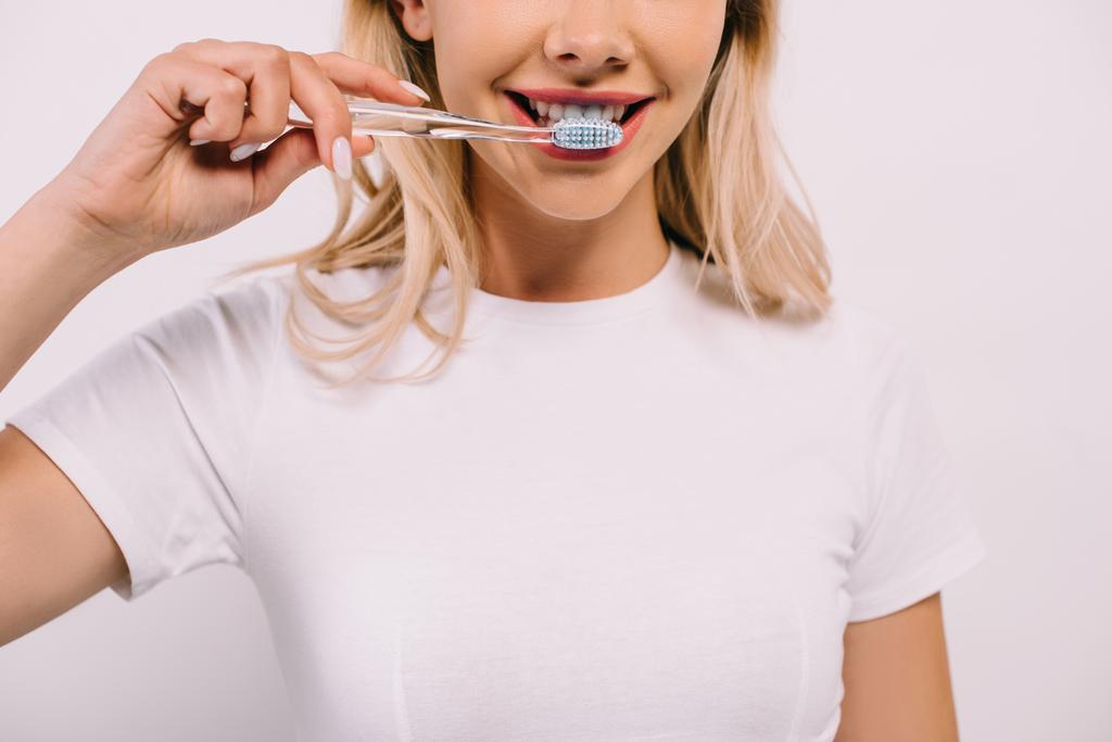 bijgesneden beeld van vrouw in witte t-shirt poetsen tanden geïsoleerd op wit - Foto, afbeelding