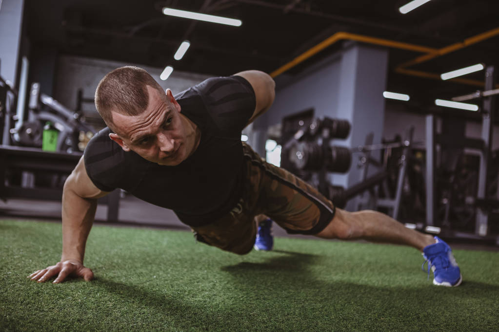 Low angle shot of a muscular athletic sportsman doing one hand pushups at the gym, copy space. Determined fitness man in sportswear exercising at the gym, doing one arm pushups - Photo, Image